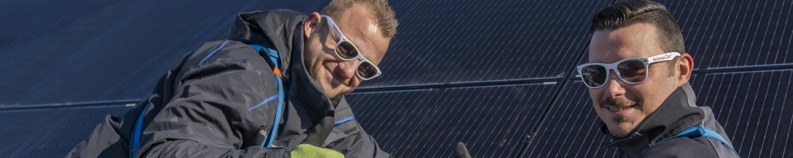 Twee mannen die zonnepanelen leggen op een dak met de duim omhoog