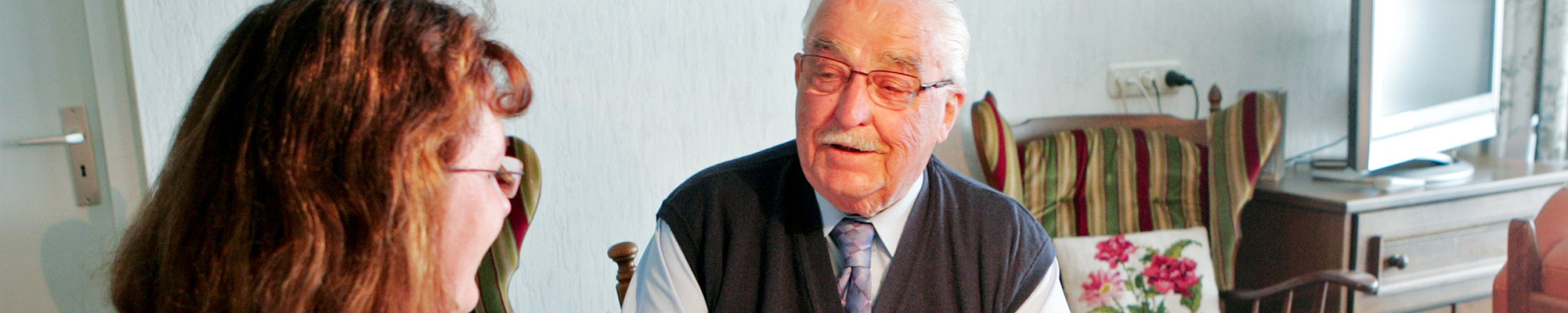 zorgmedewerker in huiskamer in gesprek met een oudere man