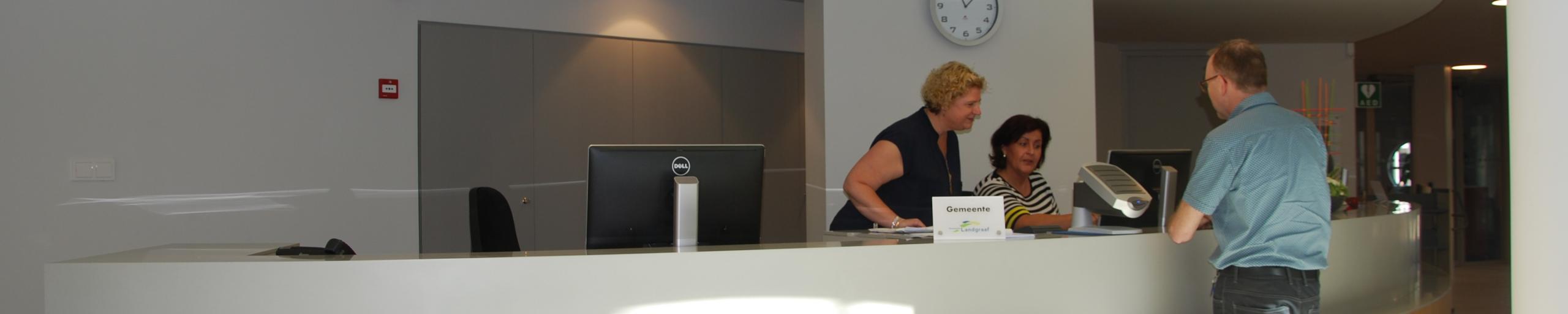 Een man aan de receptie van het Burgerhoes wordt geholpen door twee medewerkers